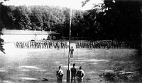The retreat formation
                  one summer evening in 1941 at Camp Morgan. The
                  military style formation with the men "At
                  Ease" suggests this photo might have been taken
                  just before the lowering of the flag. With the playing
                  of the National Anthem and flag-lowering, the men
                  would be at "Attention" and the leaders at
                  "Present Arms" saluting the flag. Note the
                  flag ropes are separated and perhaps being made ready
                  for action.