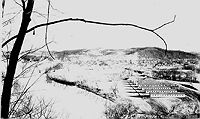 Camp buildings and general site of Camp Crawford. The bridge to town and buildings of Elizabeth are in the background.  Note the lettering and numerals,"Co 1512 CCC" on the rooftop of the foreground barracks roof.